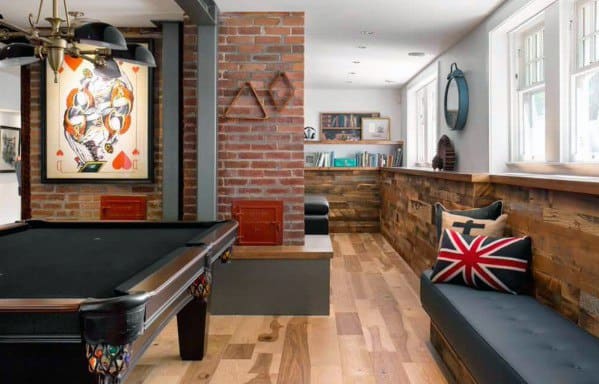 A game room with a pool table, brick wall, artwork, bench seating, and decorative pillows