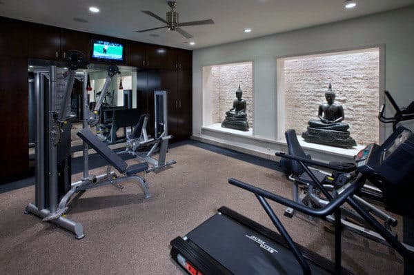 Home gym with exercise equipment, TV, and Buddha statues in wall niches for a serene home workout