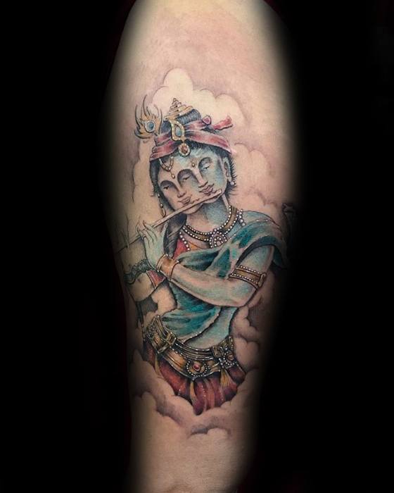 Softly colored Krishna tattoo showing him playing the flute while emerging from clouds, dressed in blue and red with delicate detailing.