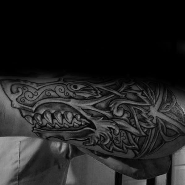 Black and white forearm tattoo of an intricately designed Celtic wolf with sharp fangs and swirling patterns.