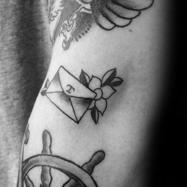 Tattoo of an envelope, flower, and letter "T" on a person's arm