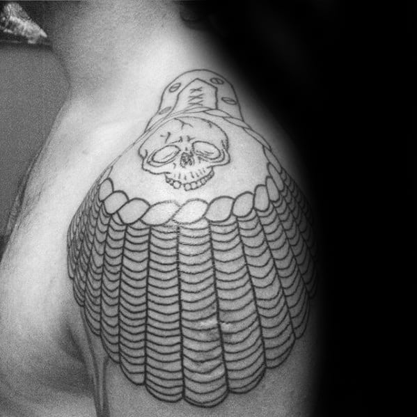 Bold epaulette tattoo with a skull centerpiece and layered scale-like tassels extending over the upper arm.