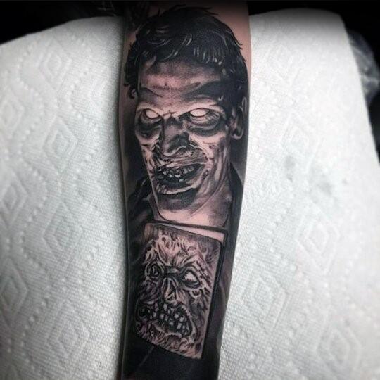 Black and grey Evil Dead tattoo of a sinister undead face with glowing eyes above a haunting Necronomicon book illustration.