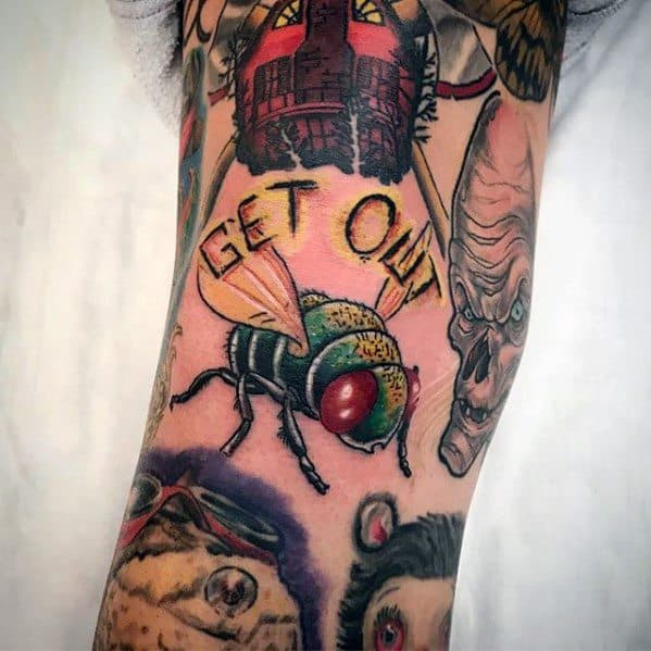 Bold fly tattoo with vibrant red eyes and green body, surrounded by horror-themed art and the phrase "GET OUT" in yellow text.