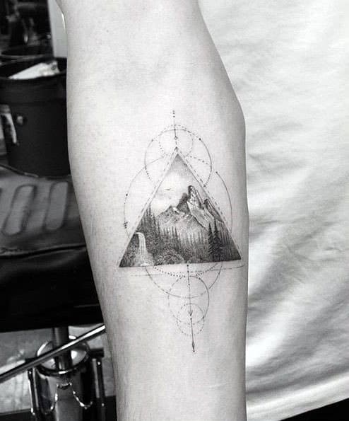 Forearm tattoo of a mountain landscape inside a triangle, surrounded by symmetrical geometric dot and line patterns.
