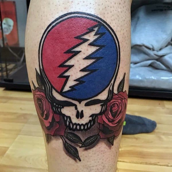 Grateful Dead Steal Your Face skull tattoo with red and blue lightning bolt and detailed roses beneath the skull on the calf.