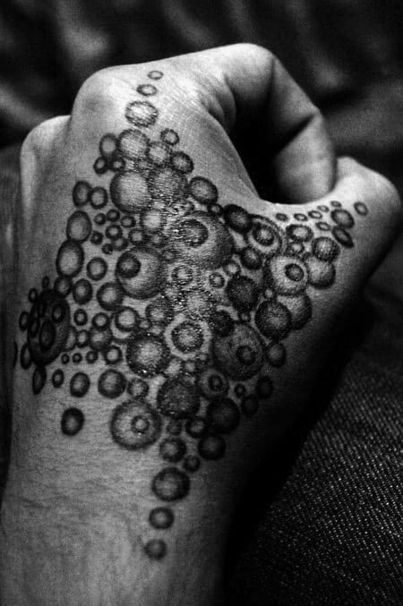 Black and white tattoo of overlapping circles and bubbles, creating a textured, organic pattern that flows across the hand, with varying shades of grey for depth and contrast.