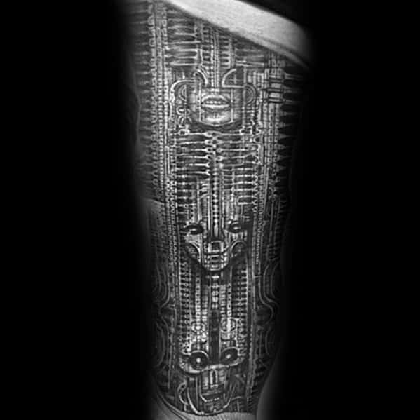 HR Giger-style biomechanical tattoo featuring elongated alien faces interwoven with intricate mechanical spine and circuit-like structures.