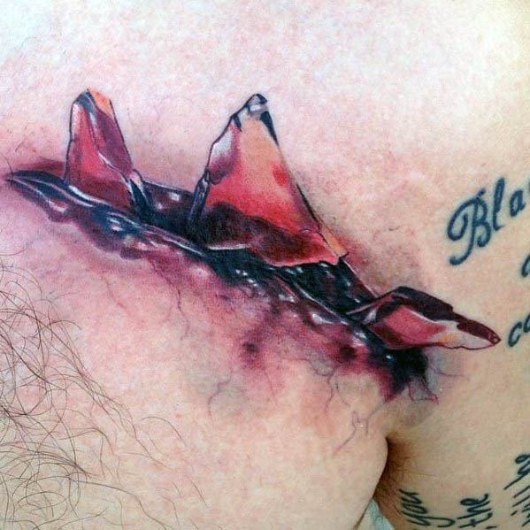 Hyper-realistic tattoo of sharp glass shards appearing to pierce through the skin, with vivid red tones and a raw, torn flesh effect.