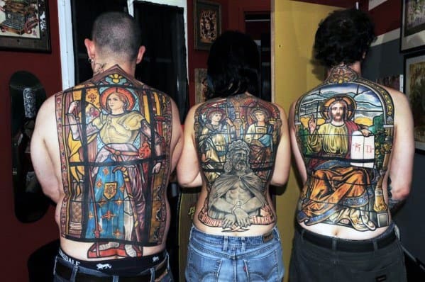 Full-back stained glass-style tattoos on three individuals, featuring Joan of Arc, religious imagery, and medieval-inspired designs.