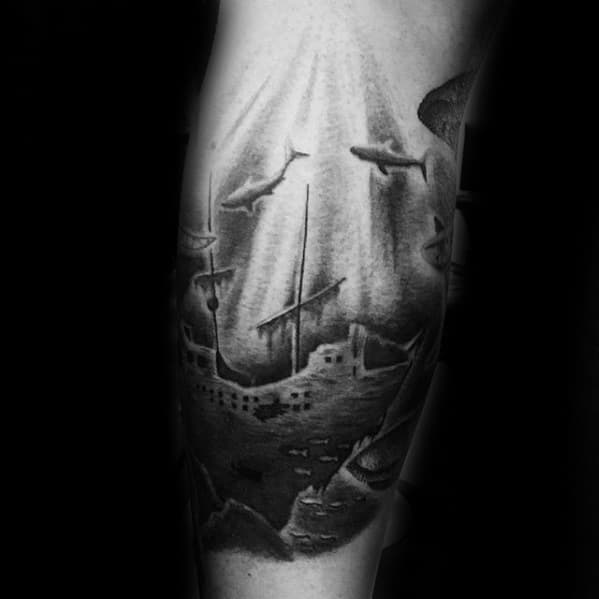 Black and grey underwater shipwreck tattoo with sharks swimming above a sunken vessel illuminated by rays of light from the surface.