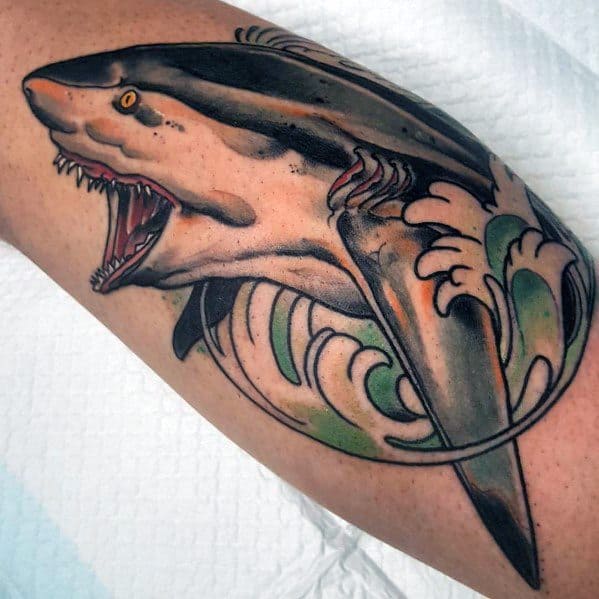 Neo-traditional shark tattoo with an open jaw, bold outlines, and stylized ocean waves in green and cream tones.