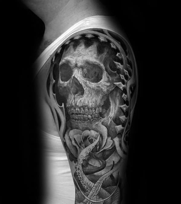 Tattoo of a skull with roses and tentacles on a person's upper arm in black and white