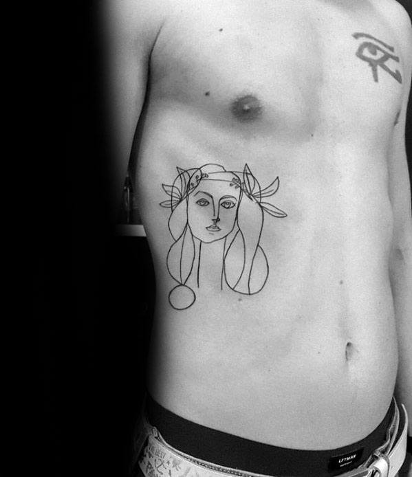 Ribcage tattoo of a Picasso-style female face with floral elements, drawn in fine linework and soft, abstract features.
