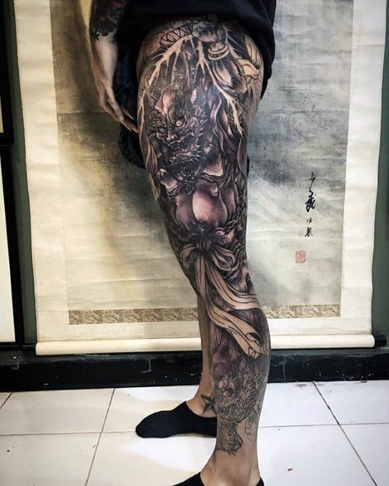 Dark Raijin leg sleeve tattoo in black and grey tones, featuring fierce thunder god with flowing ribbons and intense shading.