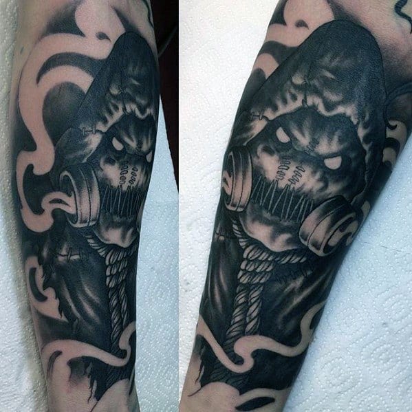 Menacing scarecrow tattoo with glowing eyes, gas mask, rope neck, and swirling smoke, inked in dark black and grey tones.