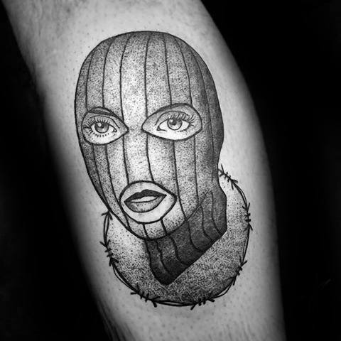 Tattoo of a ski mask with feminine eyes and lips, surrounded by barbed wire in a circular pattern.