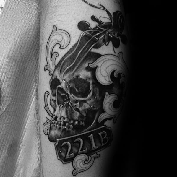 Tattoo of a skull with a violin scroll and "221B," surrounded by decorative swirls