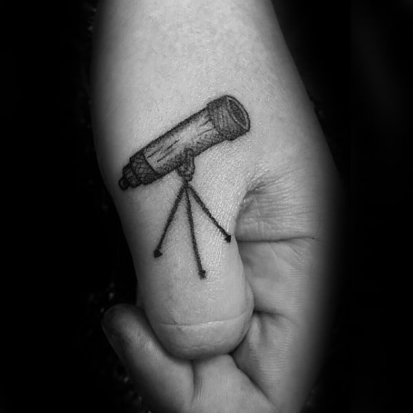Close-up of a thumb tattoo featuring a telescope in black and white