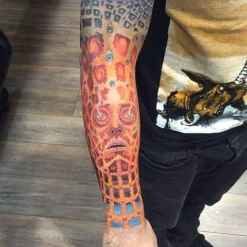 Full-sleeve Tool-inspired tattoo with a symmetrical red and orange pattern, featuring a stylized face and abstract geometric shapes.