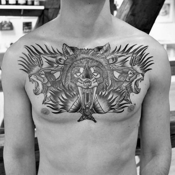 Bold chest tattoo featuring a roaring bear head, crossed torches, and mirrored wolves with detailed tribal and flame-like accents.