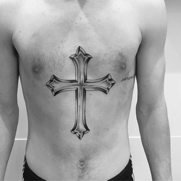 Large 3D-style ornamental cross tattoo in black and grey ink centered on the chest, with beveled edges and bold shading.