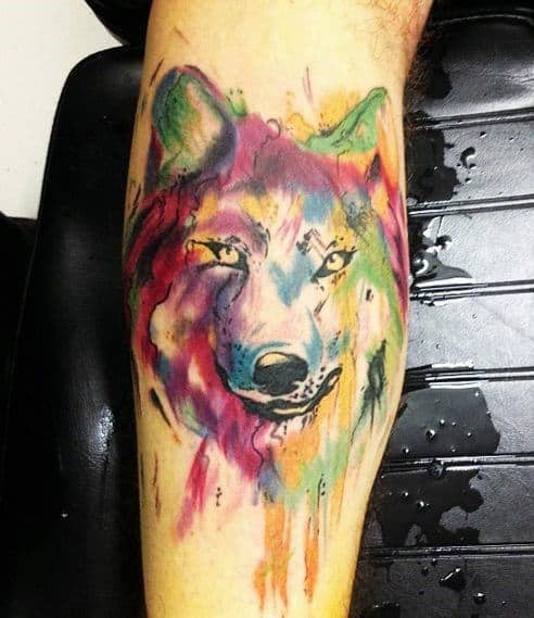 Vibrant watercolor wolf tattoo with multicolor splashes and dripping ink effect, blending fierce gaze with artistic chaos.