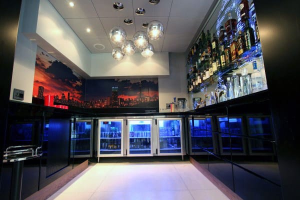 Sleek bar interior with modern lighting, illuminated liquor shelves, and a vibrant cityscape mural