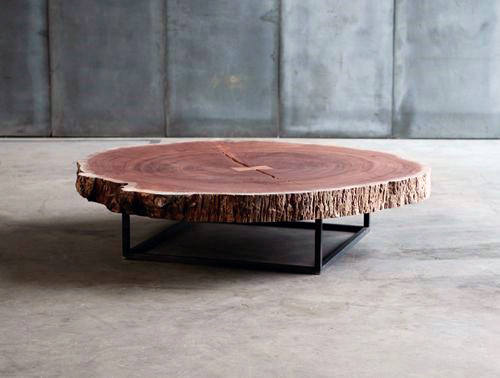 Round wooden coffee table with a natural edge and metal legs on a concrete floor