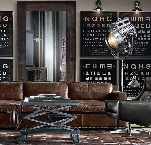Industrial-themed living room with leather sofas, eye chart wall art, and a large spotlight fixture