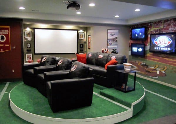 Man cave home theater with sports team-themed decor, black chairs, a large screen, and wall-mounted TV displays