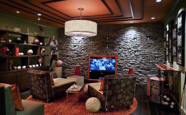 Cozy man cave with patterned chairs, TV, sports memorabilia, and stone accent wall under warm lighting
