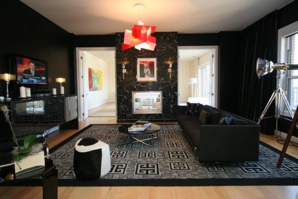 Modern man cave living room with black walls, patterned rug, black sofa, large window, and contrasting red ceiling light