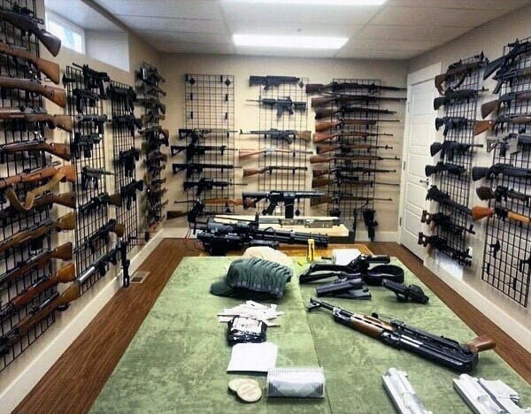 Spacious gun room with grid wall racks showcasing rifles and firearms, complemented by a central workspace.