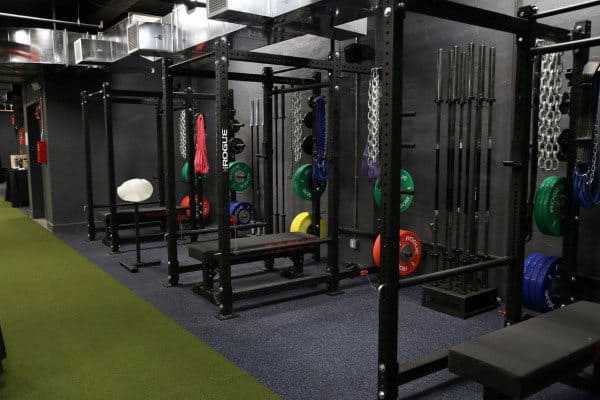 Home gym with squat racks, colorful weight plates, benches, and hanging chains on rubber flooring