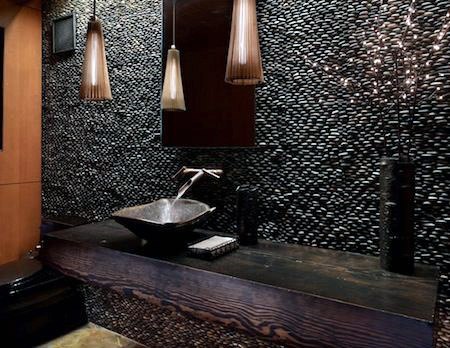 Elegant bathroom with stone sink, modern faucet, and pebble wall with hanging lights
