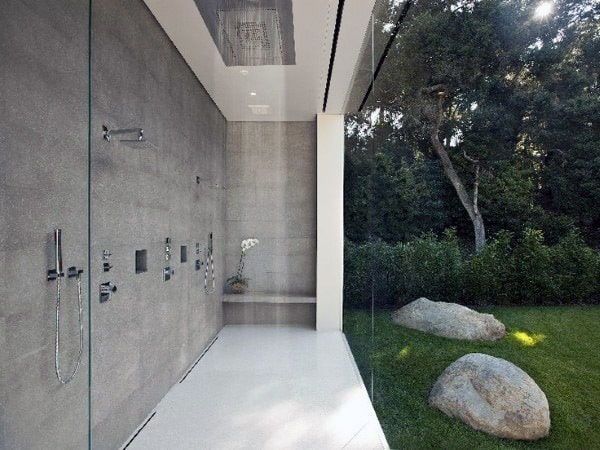 Modern glass shower with stone walls offers a serene view of lush greenery outside
