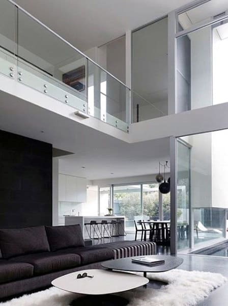 Contemporary living room with black sofa, glass railing, and open kitchen dining area.