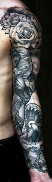 Tattooed arm with roses, a skull, and a shark design in black and gray ink