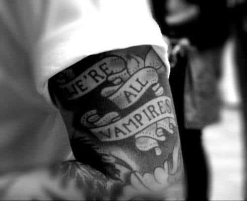 Black and white tattoo on arm reads "We're all vampires"