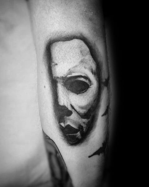 Minimalist black and grey Michael Myers tattoo with a shadowy, eerie mask design for a subtle yet haunting effect.