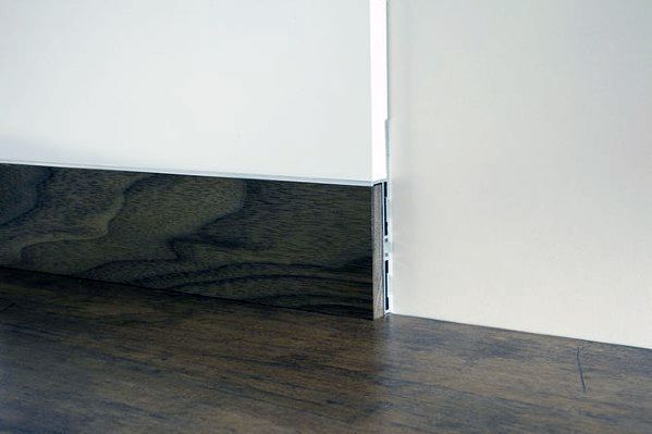 Dark wood baseboard with minimalist design against white walls and matching wood flooring.
