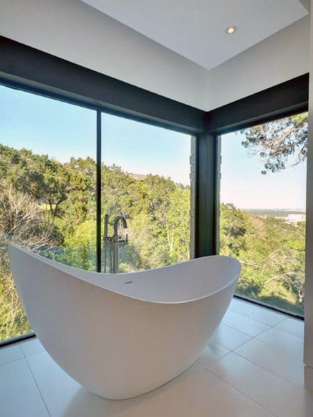 Freestanding bathtub near large windows with a scenic outdoor view of trees