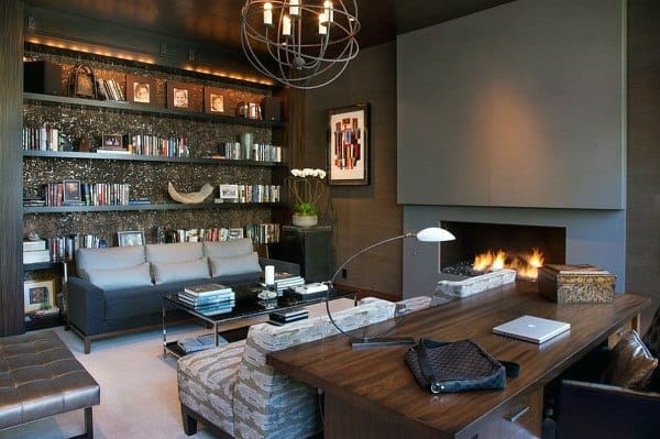 Modern home office with fireplace, dark wood desk, bookshelves, and cozy seating area.