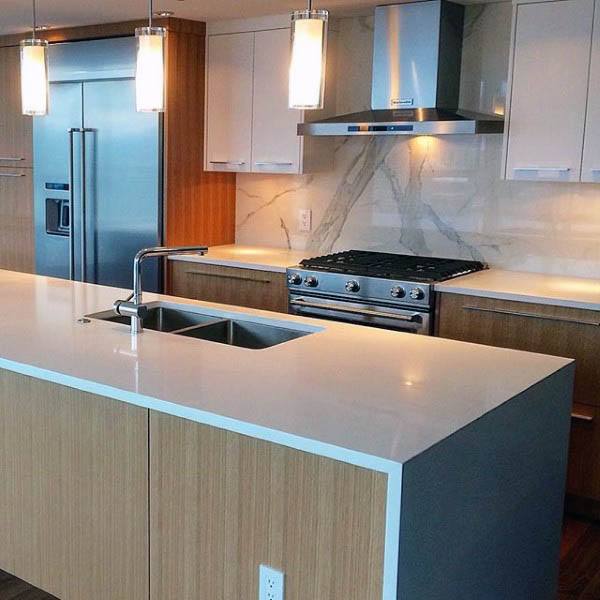 Modern kitchen with wood-paneled cabinets, marble backsplash, island sink, and pendant lights.