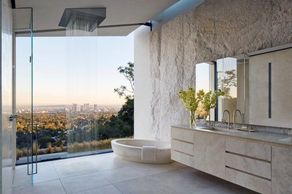 Modern bathroom with large window view, sleek fixtures, a round tub on stone floor, and a stylish shower