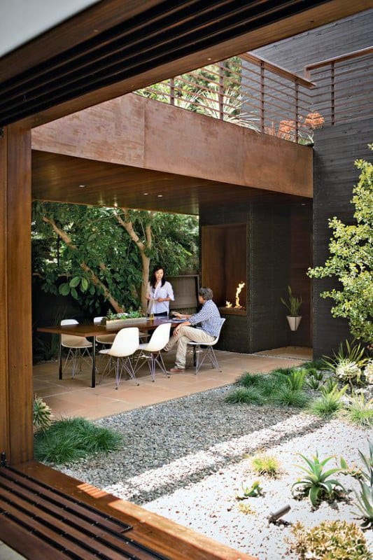 Modern patio with people sitting around a table, surrounded by greenery and wooden architecture