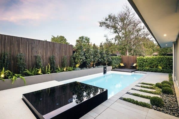 Modern backyard with a sleek pool, adjacent seating area, and landscaped greenery under a cloudy sky