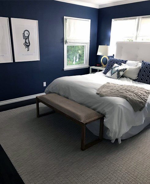 Cozy navy bedroom with white bedding, wall art, and a wooden bench at the foot of the bed.