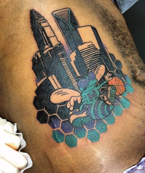 Tattoo of skyscrapers with a cartoon hornet playing basketball and hexagonal shapes in the background